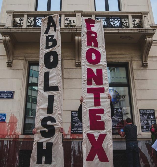 foto van actie bij frontex kantoor in brussel. 2 mensen houden 2 verticale banners op waarop "Abolish" "Frontex" staat.